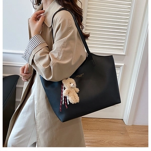 Model carrying a black leather tote bag with a cute plush bear charm for casual daily wear