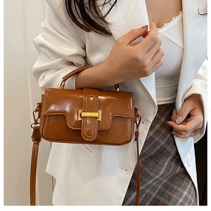 Sac à bandoulière en similicuir marron avec boucle dorée porté à l'épaule en détail