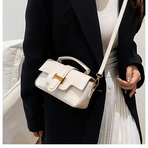 Détail d'un sac à main en cuir verni blanc crème avec boucle dorée sur blazer noir
