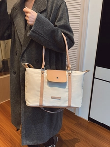 Large beige canvas tote bag with brown leather trim carried by a model in a wool coat