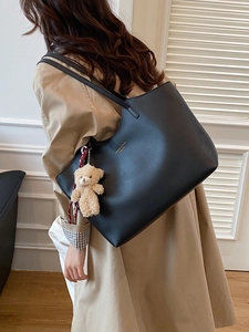 Chic black soft leather tote bag with bear charm carried by model in trench coat