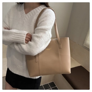 Detail of a beige leather tote bag featuring modern typography and slim dual shoulder straps