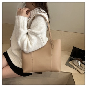 Detail of minimalist beige tote bag with fine stitching and gold logo on leather