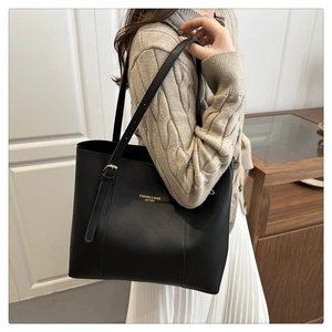 Macro view of matte black leather tote with gold logo and adjustable shoulder strap buckle