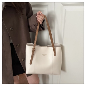 Detail of minimalist cream tote bag showing brown straps and golden brand lettering