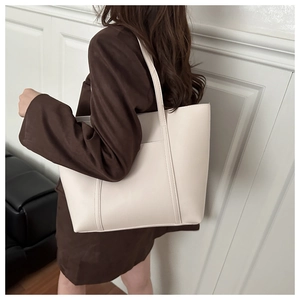 Detailed view of cream-colored tote bag in matte leather being worn by a model