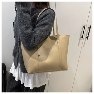 Detailed view of beige faux leather tote bag with U-shaped stitching and tassel charm
