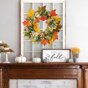 Autumn harvest wreath with orange maple leaves and white pumpkins on a fireplace window