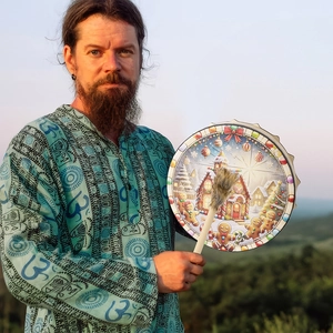 Close-up of shaman drum with gingerbread house pattern and drumstick in sunset forest