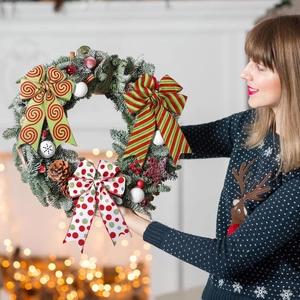 Christmas wreath with festive ribbons pine cones and berries held by a woman in a sweater