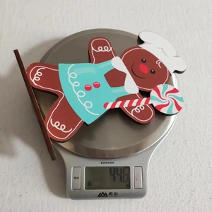 Detail view of a 44.6g wooden gingerbread man figurine holding a candy cane on a scale
