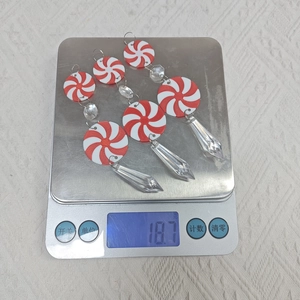Three red and white candy cane pendants with crystal drops being weighed on a scale