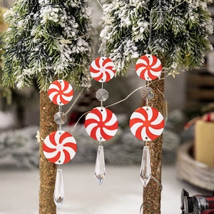 Red and white Christmas candy ornaments with crystal beads hanging on snowy pine tree