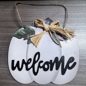 Close-up of white wooden pumpkin welcome sign with green leaves and straw bow decor