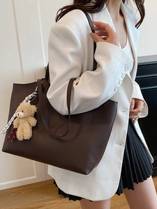 Brown leather tote bag with plush bear charm and striped scarf shown on model