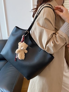 Large black matte leather tote bag with gold hardware and plush bear charm on model