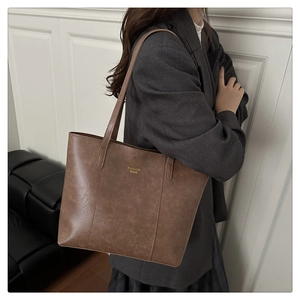 Close-up of a large dark brown tote bag with vintage leather texture and gold text
