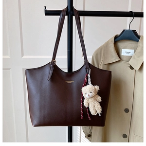 Detail of dark brown tote bag with gold lettering and cute plush bear charm accessory