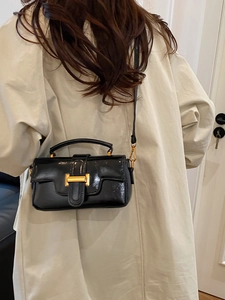 Sac bandoulière chic en cuir verni noir avec boucle dorée porté par un mannequin