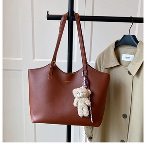 Detail of a brown leather tote bag featuring a cute teddy bear charm and fashion text