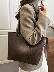 Brown faux leather tote bag with vintage texture and gold lettering on beige coat