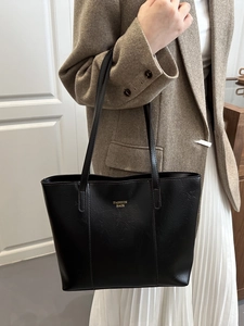 Minimalist black PU leather tote bag with gold lettering shown in a stylish fashion setting