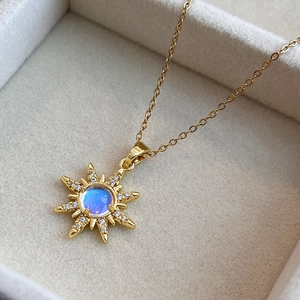 Golden sunburst necklace with central blue gemstone displayed in a beige velvet jewelry box