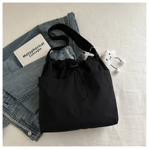 Close-up of minimalist black nylon crossbody bag with drawstring closure and cute charm