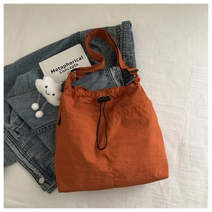 Detail view of orange nylon tote bag with drawstring closure and plush cloud charm