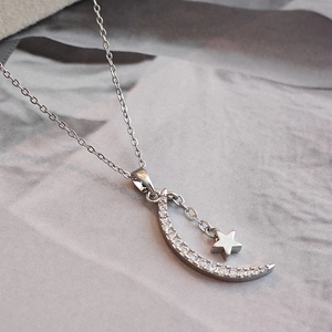Minimalist silver star and moon pendant necklace on elegant grey silk fabric background