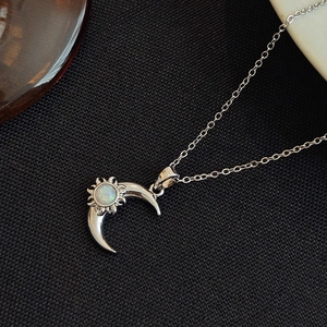 Silver crescent moon and sun necklace with glowing white opal stone on black fabric