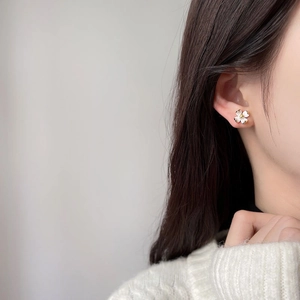 Élégantes boucles d'oreilles fleurs en émail blanc avec bordure dorée portées par un mannequin