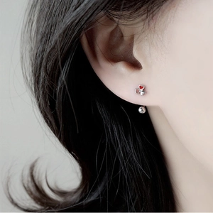 Gros plan d'une boucle d'oreille trèfle asymétrique en argent avec pétale de cœur rouge