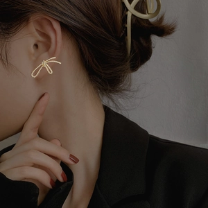 Détail de boucles d'oreilles nœud dorées avec texture scintillante portées par un mannequin