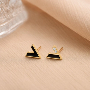 Détail de boucles d'oreilles asymétriques en V dorées avec émail noir et zircons