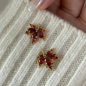 Détail d'une broche en forme de feuille d'érable dorée avec gemmes rouges sur un pull