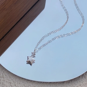 Detailed close-up of a silver star pendant necklace reflected on a clean round mirror