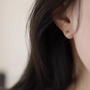 Close-up of a square red zircon stud earring with milgrain gold edge on a female ear