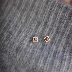 Macro shot of square red zircon stud earrings with micro-pave crystals on grey sweater