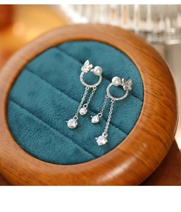 Détail de boucles d'oreilles papillon avec perles et longs glands sur fond en velours vert