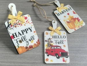 Close-up of three wooden autumn hanging tags with pumpkin designs and plaid bows