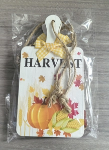 Close-up of harvest decorative wooden sign with yellow plaid bow in plastic packaging