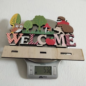 Detail of wooden welcome sign with autumn animals on a scale showing 53.2g weight