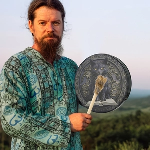 Close-up of a dark shamanic drum featuring a black cat and magic book design in nature