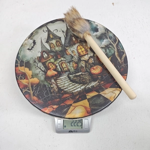 Macro detail of Halloween decorative drum showing haunted castle graphics and a wooden brush