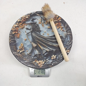 Detailed view of Shaman drum with witch print and mallet on a scale showing 218g weight
