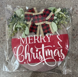 Detail view of a round Christmas wooden door sign with a red plaid bow and green foliage