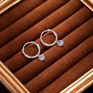 Détail de créoles torsadées en argent avec breloques zircon sur velours marron