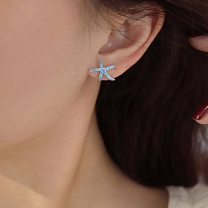 Blue starfish stud earrings with crystal pavé on silver metal shown on model's ear
