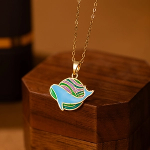 Detailed close-up of a blue enamel whale and planet pendant on a golden chain necklace